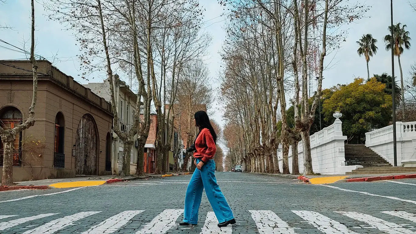 Uma mulher atravessando uma faixa em uma rua de paralelepípedos no Centro Histórico de Colonia do Sacramento.