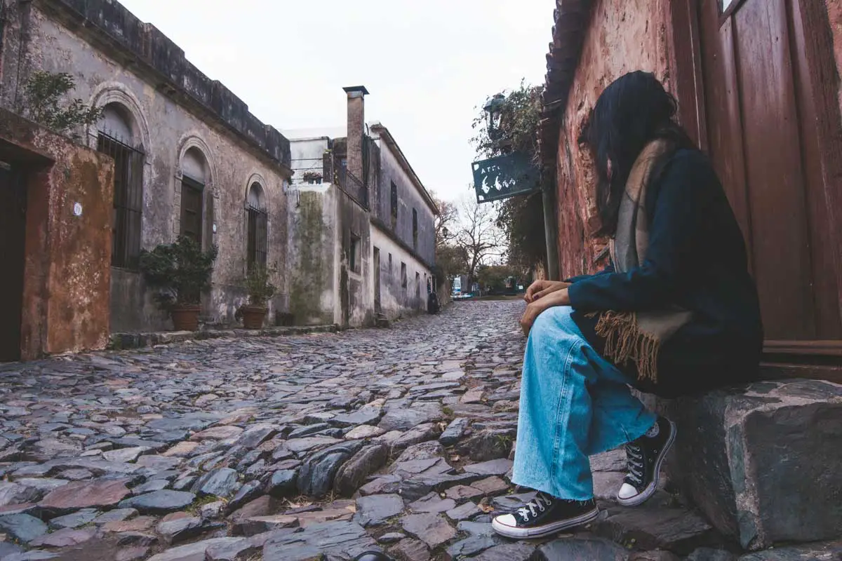 Mulher sentada, contemplando a encantadora Calle de los Suspiros em Colonia del Sacramento.