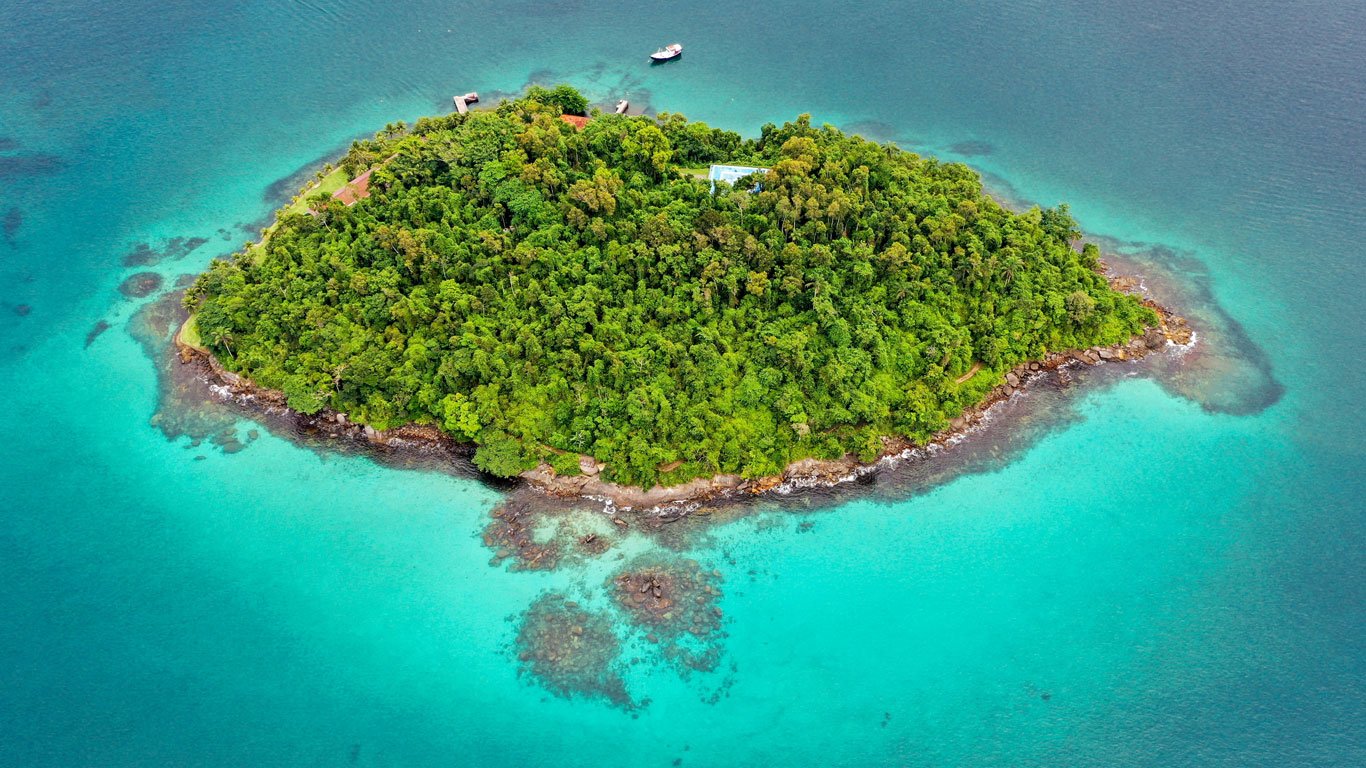 Vista aérea de uma pequena ilha coberta pela mata atlântica, perdida no oceano de águas turquesa em Angra dos Reis, um dos melhores lugares para viajar no Rio de Janeiro.