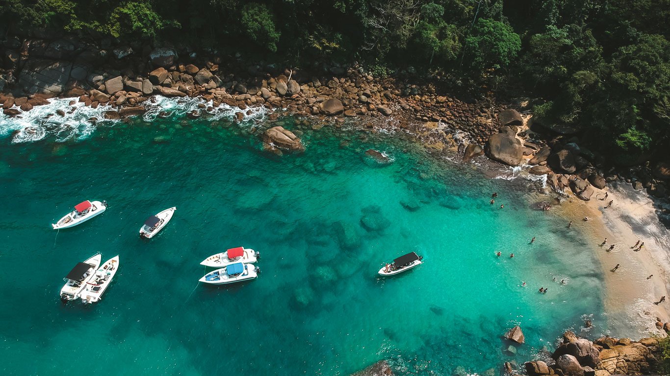 Vista aérea da Praia do Cachadaço em Ilha Grande, com barco parado sobre as águas cristalinas.