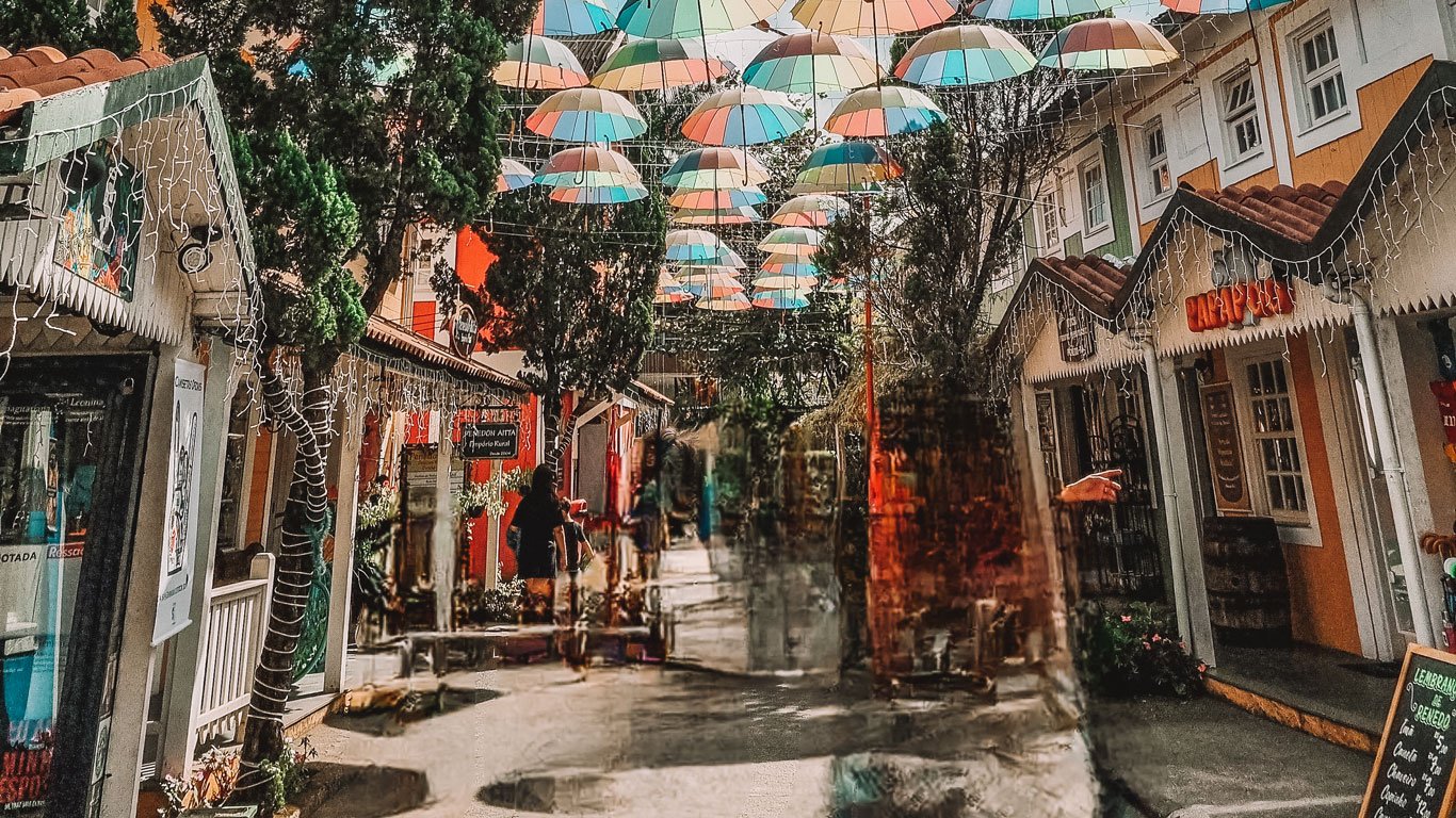 Centro de Penedo, com lojinhas coloridas e uma rua coberta de guarda-chuvas coloridos.