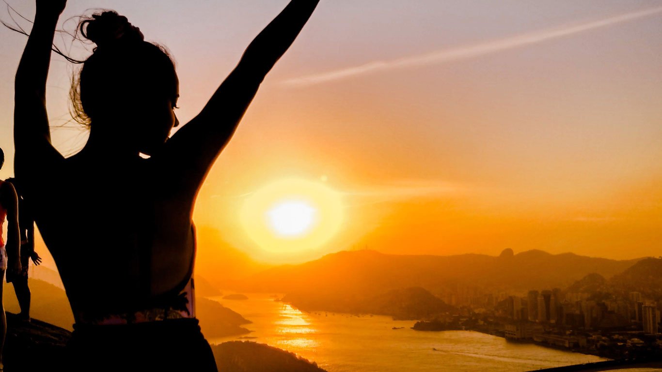 Mulher com os braços levantados, contemplando o entardecer no Morro do Moreno.