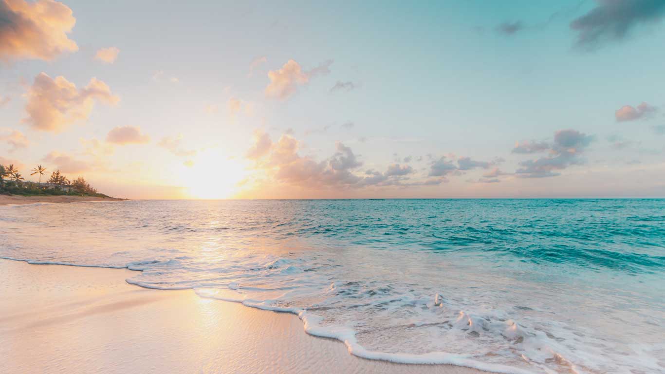 Praia paradisíaca no Havaí ao amanhecer, com a luz suave do sol refletindo na água cristalina e na areia branca. Algumas palmeiras estão ao fundo, emoldurando a cena tranquila e serena.