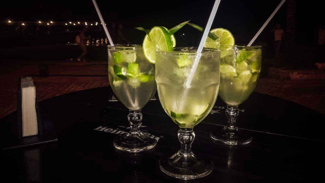 Três caipirinhas, servidas em uma taça de vidro, no Bar Zapata em Búzios. A fundo, a Orla Bardot durante ]á noite.