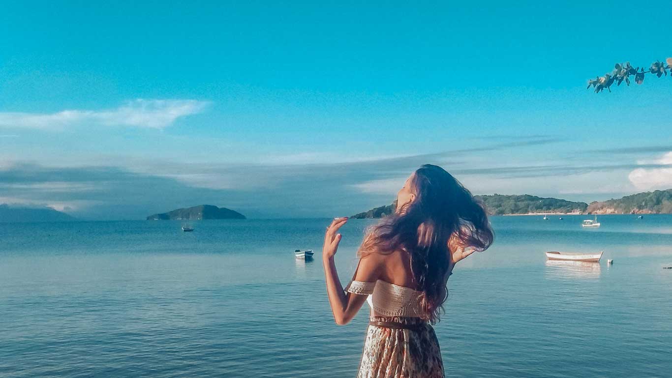 Mulher com cabelos ao vendo, em Manguinhos, admirando o mar de Búzios.