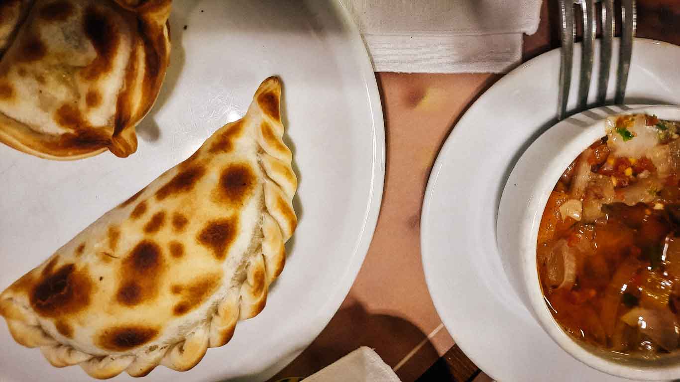 Imagem de duas empanadas uruguaias assadas acompanhadas por um molho.