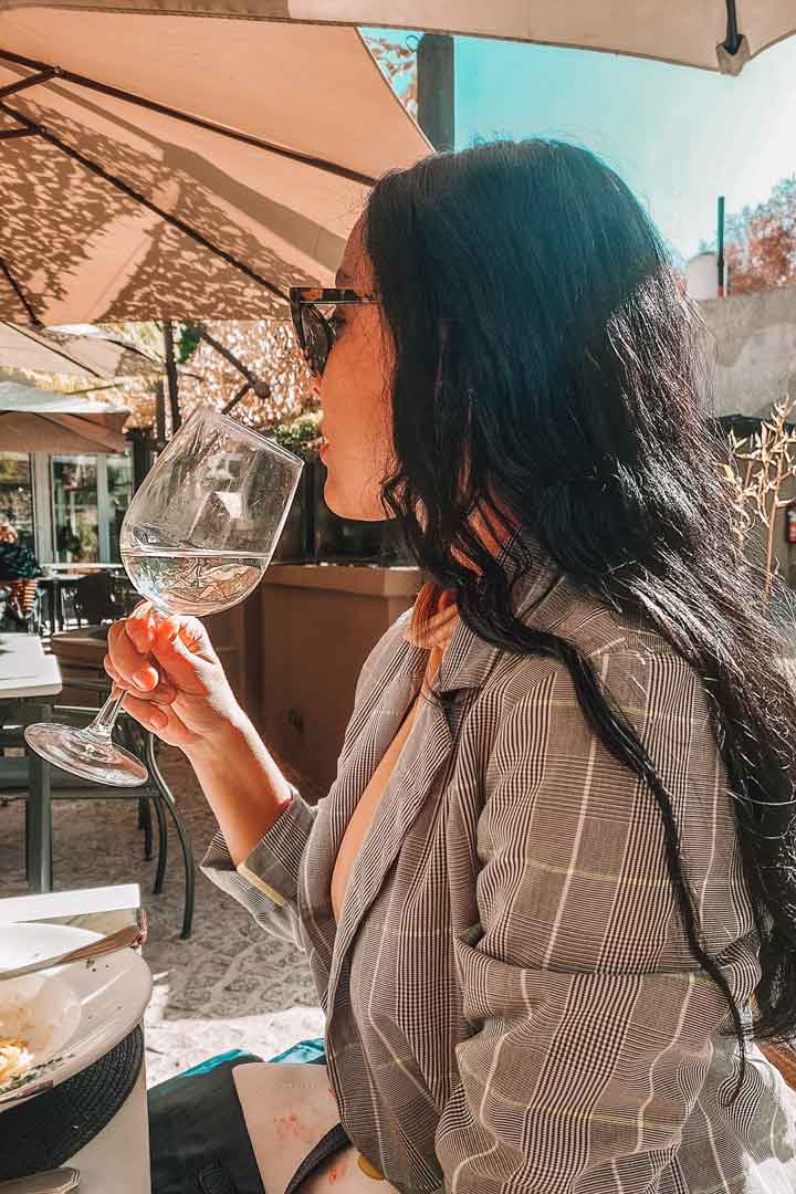 Uma mulher desfrutando de uma taça de vinho branco, iluminada pelos raios do sol.