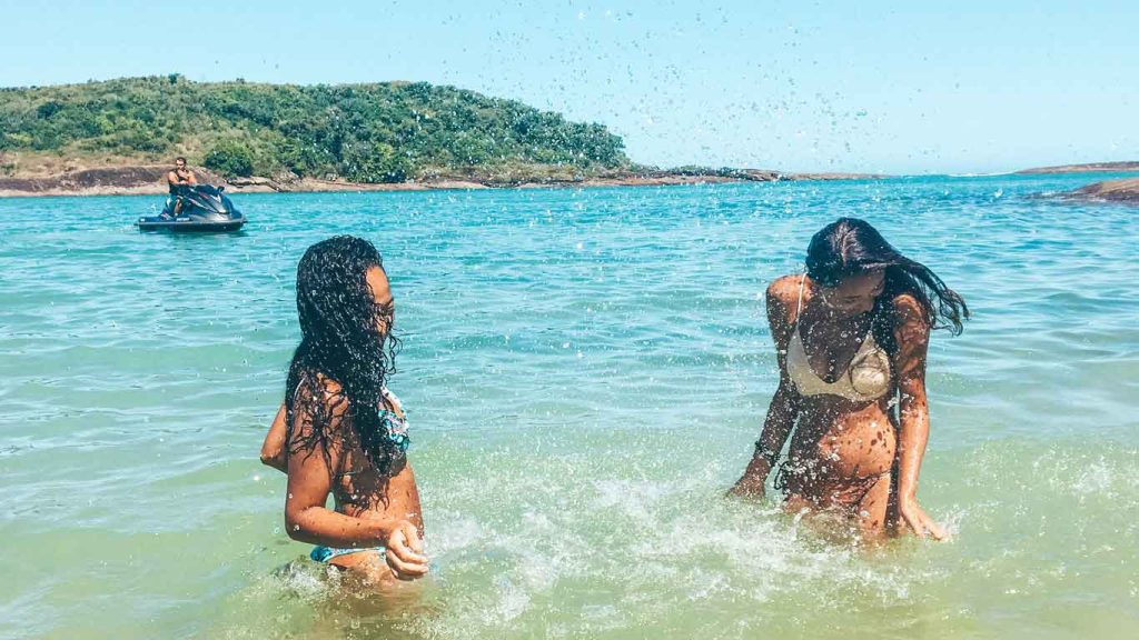 Duas mulheres brincando nas águas azuis da Praia de Bacutia em Guarapari, no Espírito Santo.