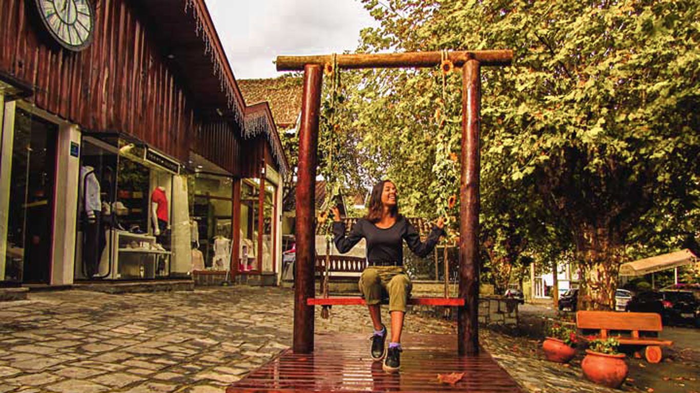 Mulher de calça verde e blusa de manga longa preta, balançando em um balanço cheio de girassóis no centro turístico de Capivari, Campos do Jordão.