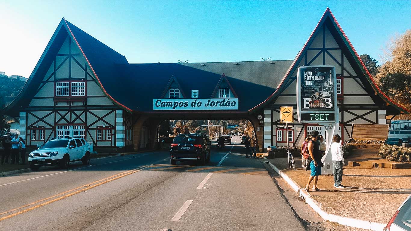 Fotografia da icônica entrada de Campos do Jordão, apresentando um edifício tradicional em estilo alpino com uma placa dizendo'Campos do Jordão' no arco. O tempo está claro. Hotéis e pousadas em Campos do Jordão com piscina aquecida.