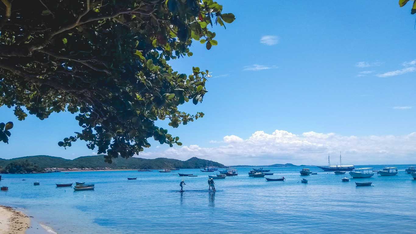 Estátua dos Três Pescadores, na Orla Bardot de Búzios, com diversos barquinhos ao fundo.