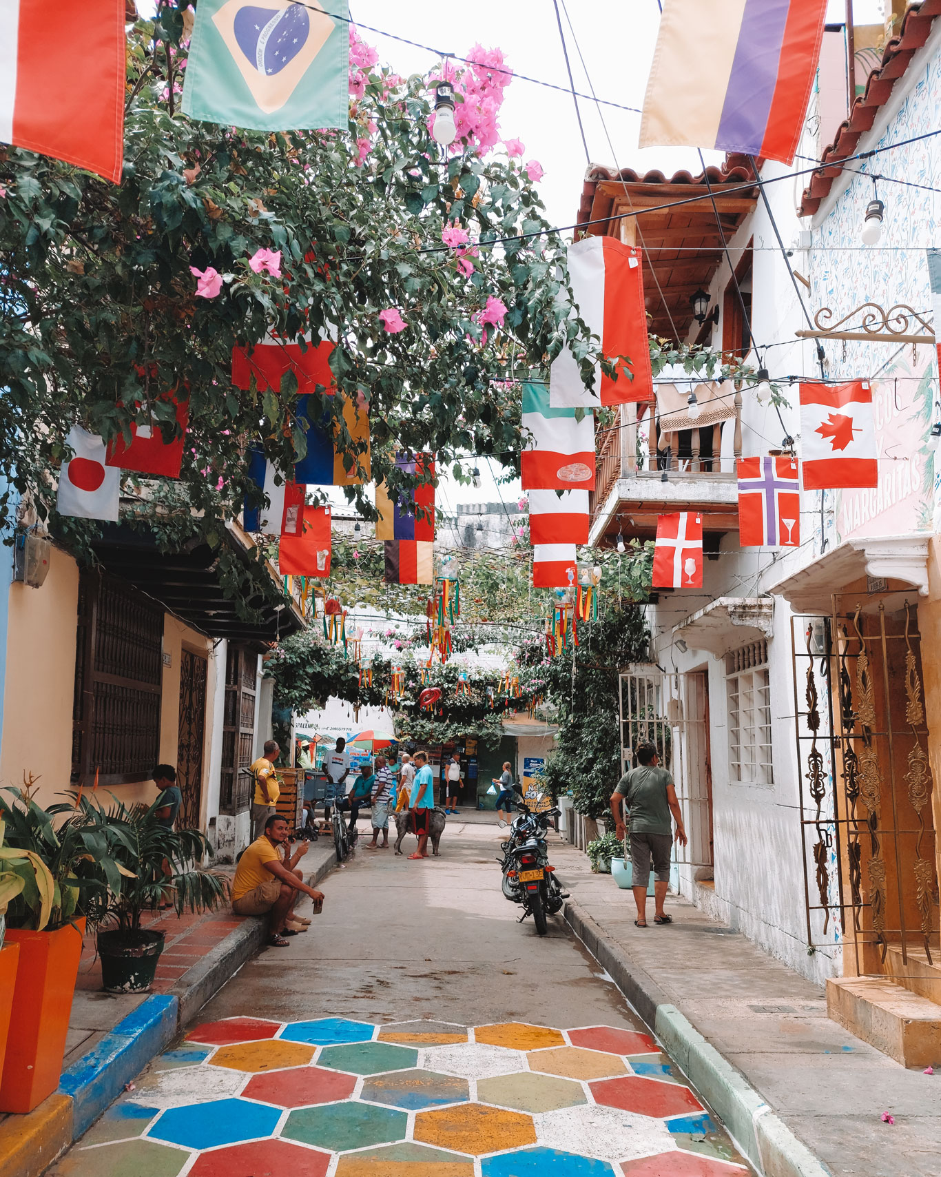 Rua estreita e colorida de Getsemaní, umas melhores opções de onde ficar em Cartagena. A rua está coberta por bandeiras de diversos países e o chão pintado de diversas cores.