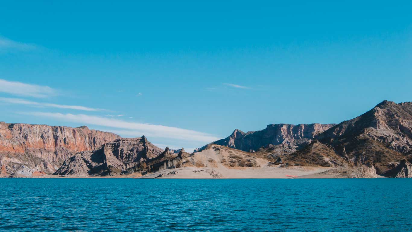 Paisagem do Cañon del Atuel, rodeado por formações rochosas em San Rafael, Mendoza, com montanhas ao fundo e um céu azul claro.