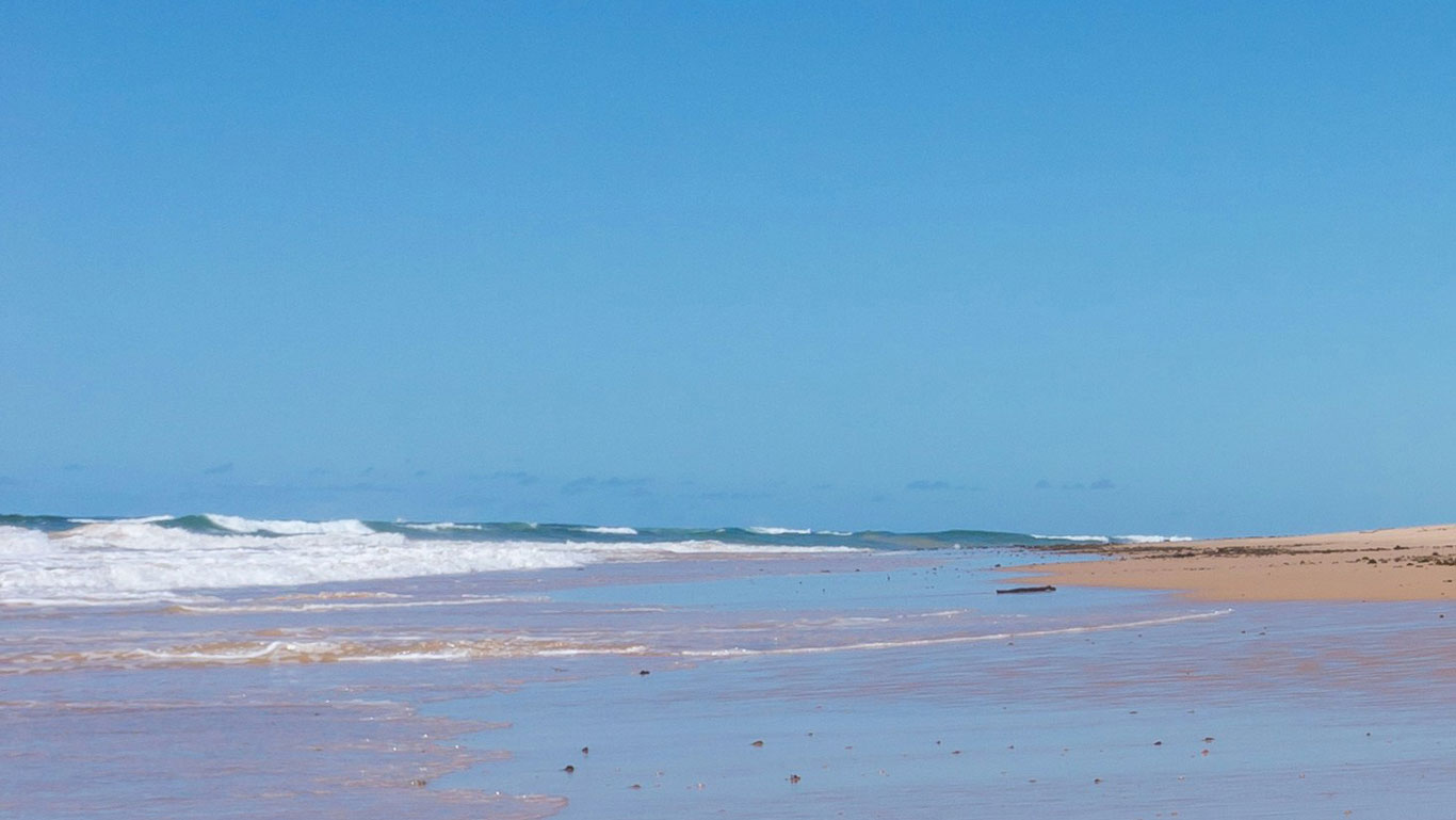 Praia da Bahia, com céu azul, areias douradas e águas azuladas.