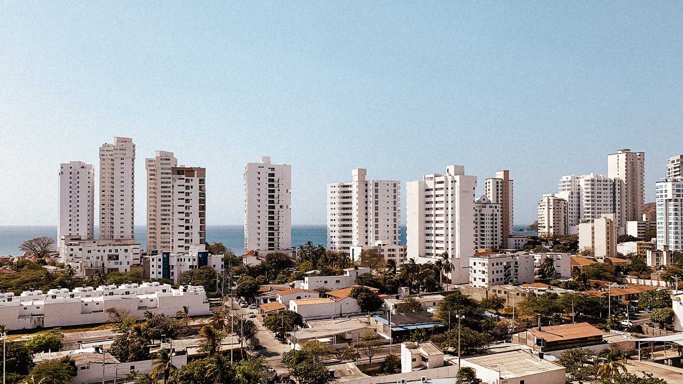 Vista panorâmica de edifícios altos próximos à praia em El Rodadero, Santa Marta. O mar aparece ao fundo, rodeado por construções modernas e um céu azul claro, no melhor bairro onde ficar em Santa Marta.