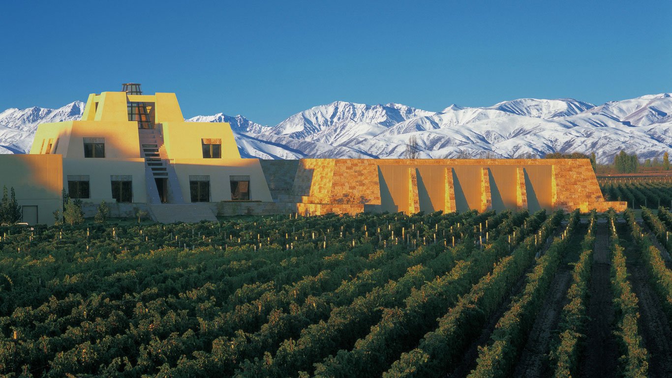 A Bodega Catena Zapata em Mendoza, Argentina, destaca-se com sua arquitetura imponente em formato de pirâmide, inspirada nas antigas construções maias, cercada por vinhedos exuberantes. Ao fundo, as majestosas montanhas dos Andes cobertas de neve realçam a beleza e a grandiosidade do local, que é uma das vinícolas mais icônicas da região.