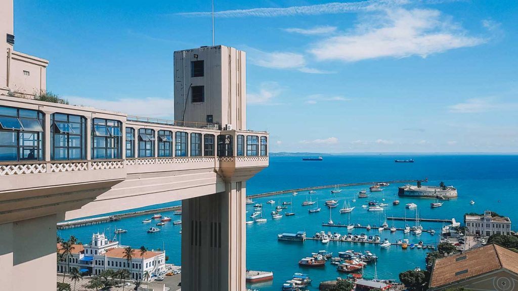 Vista do Elevador Lacerda para o mar e o céu azul. Ao fundo barcos compõem a vista no pelourinho, um das regiões mais populares onde ficar em Salvador, na Bahia.