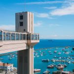 Vista do Elevador Lacerda para o mar e o céu azul. Ao fundo barcos compõem a vista no pelourinho, um das regiões mais populares onde ficar em Salvador, na Bahia.