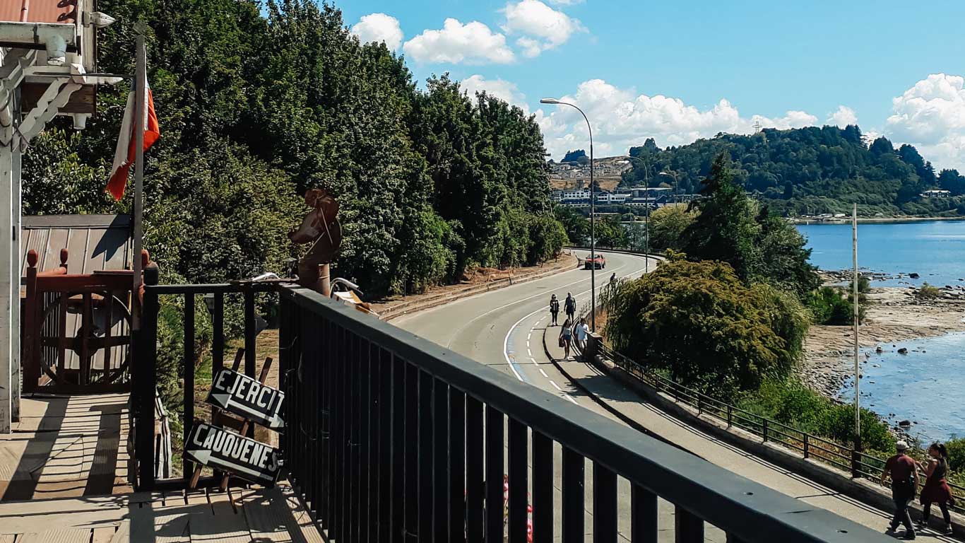 Costanera de Puerto Varas vista de uma varanda, o melhor lugar onde ficar em Puerto Varas para ter uma visão privilegiada do lago. A estrada que percorre o lago é acompanhada por árvores verdes.