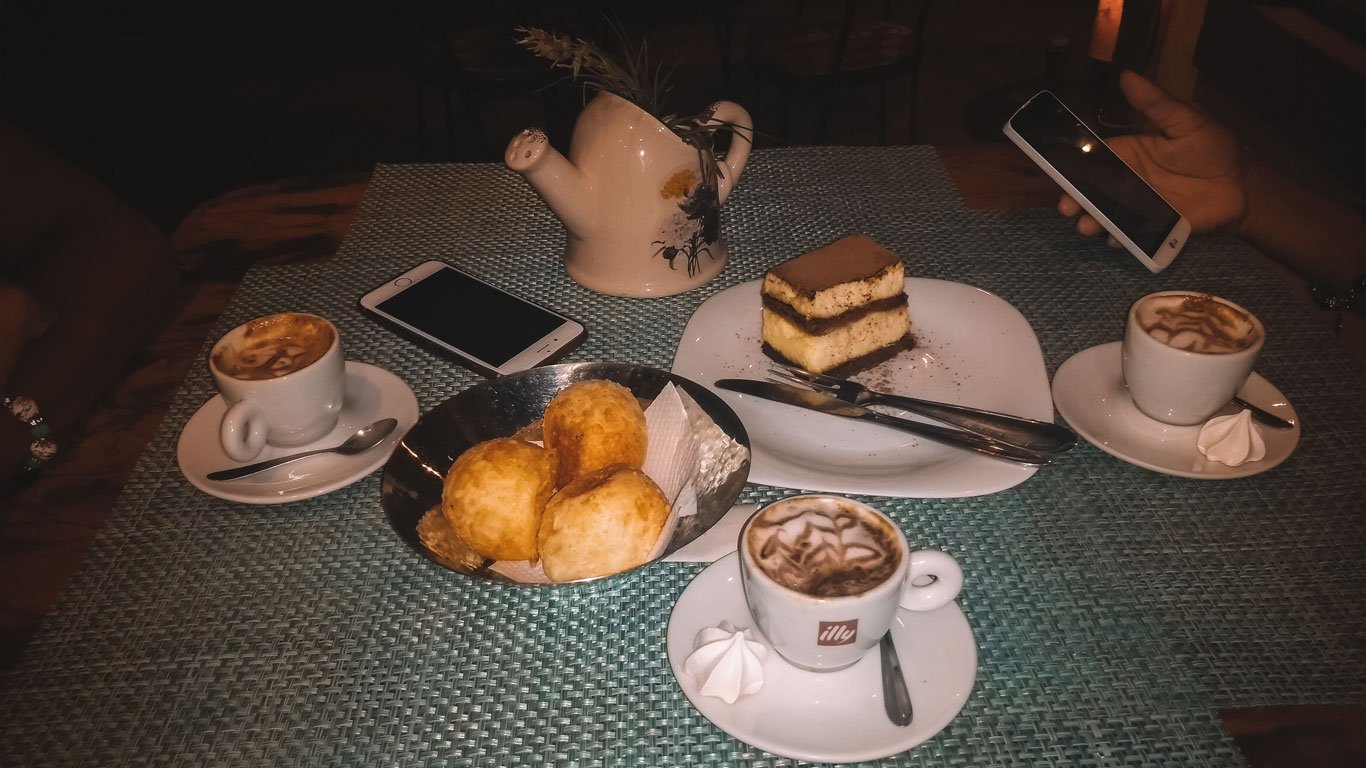 Imagem de um café com pão de queijo, torta e cappuccino servidos em uma mesa charmosa no Porto da Barra em Búzios.