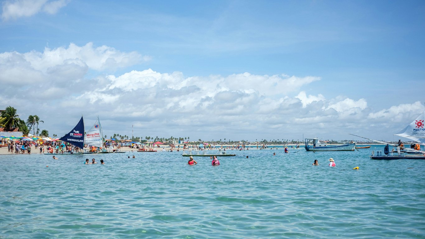 Vista da praia de Porto de Galinha em um dia ensolarado, com o mar azul e muitos banhistas.