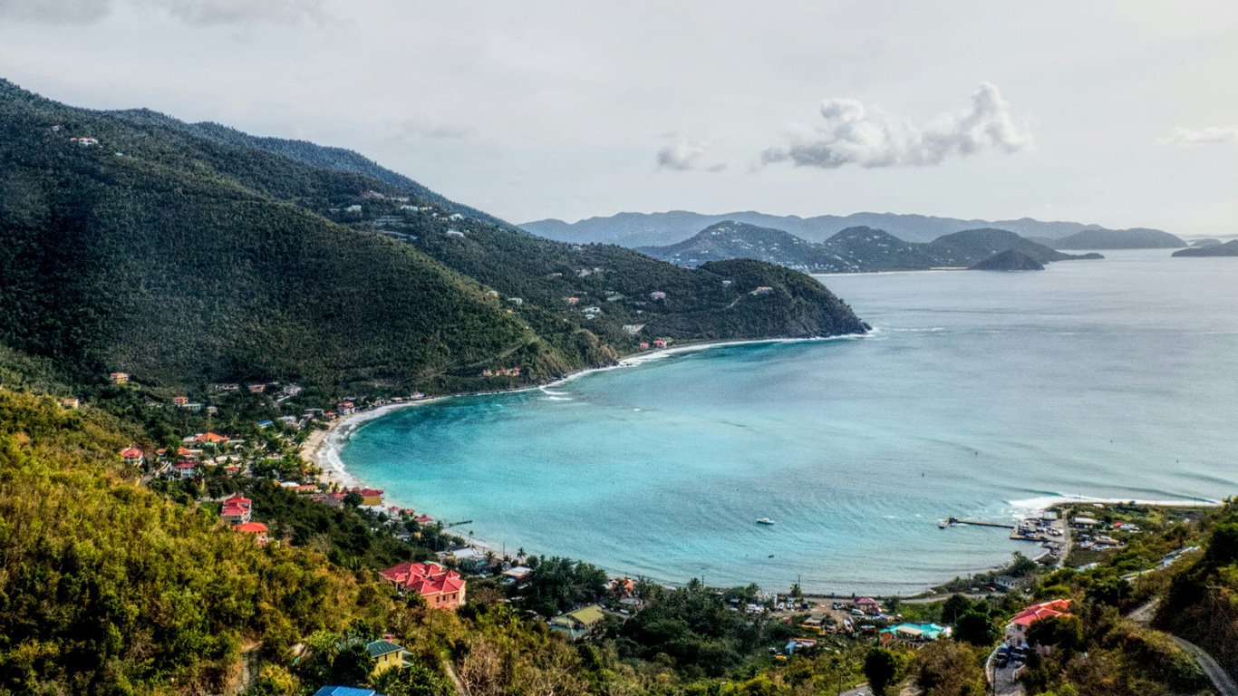 Uma baía isolada nas Ilhas Virgens Britânicas, com casas coloridas espalhadas pelas colinas e um mar calmo cercado por vegetação luxuriante.