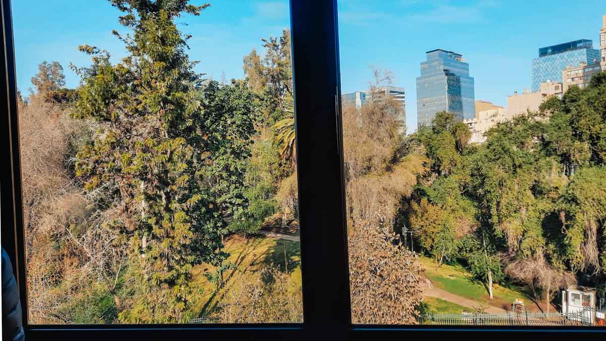 Vista do Foresta Hotel no bairro Lastarria, mostrando a vegetação exuberante do Cerro Santa Lucia em Santiago, com edifícios modernos ao fundo.