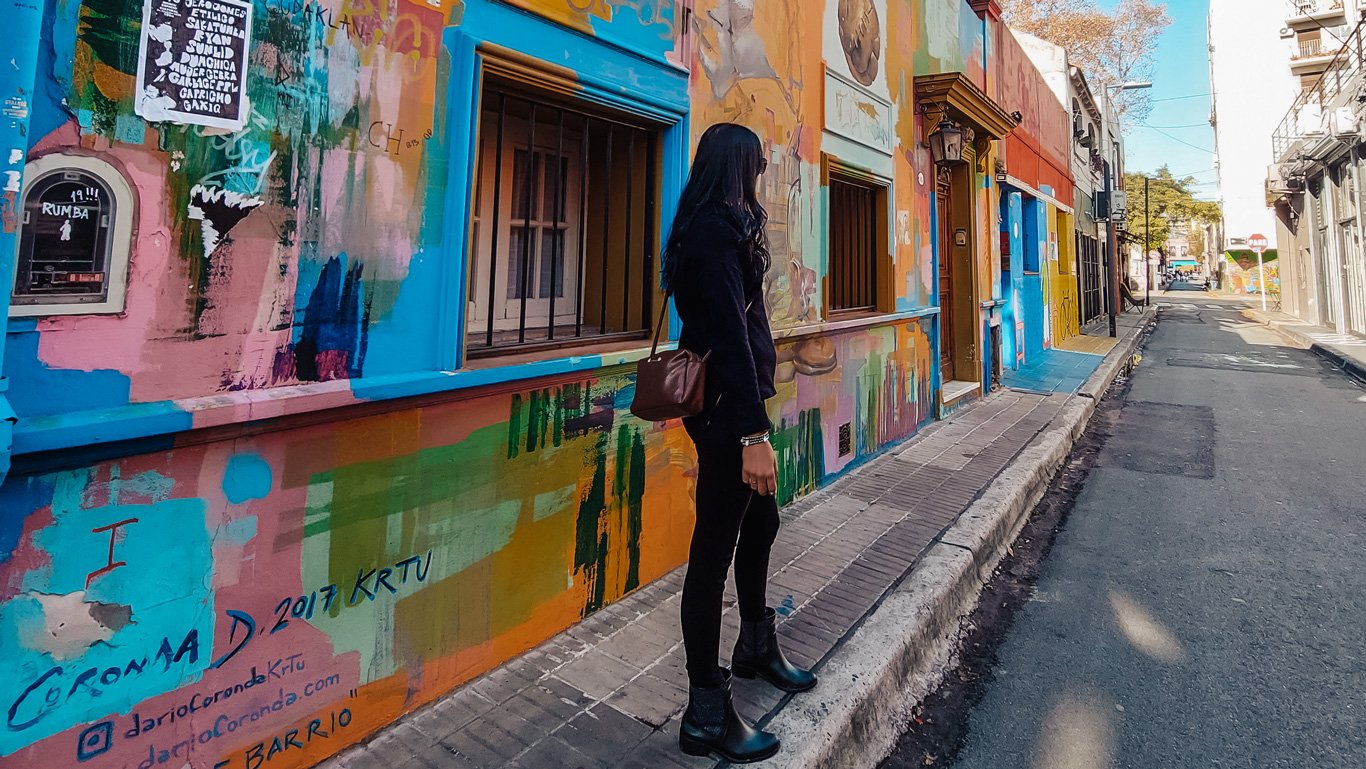 Mulher vestindo uma roupa de frio preta, posando para uma foto de forma descontraída na Calle Russel, uma rua com muitas artes de rua em Palermo.