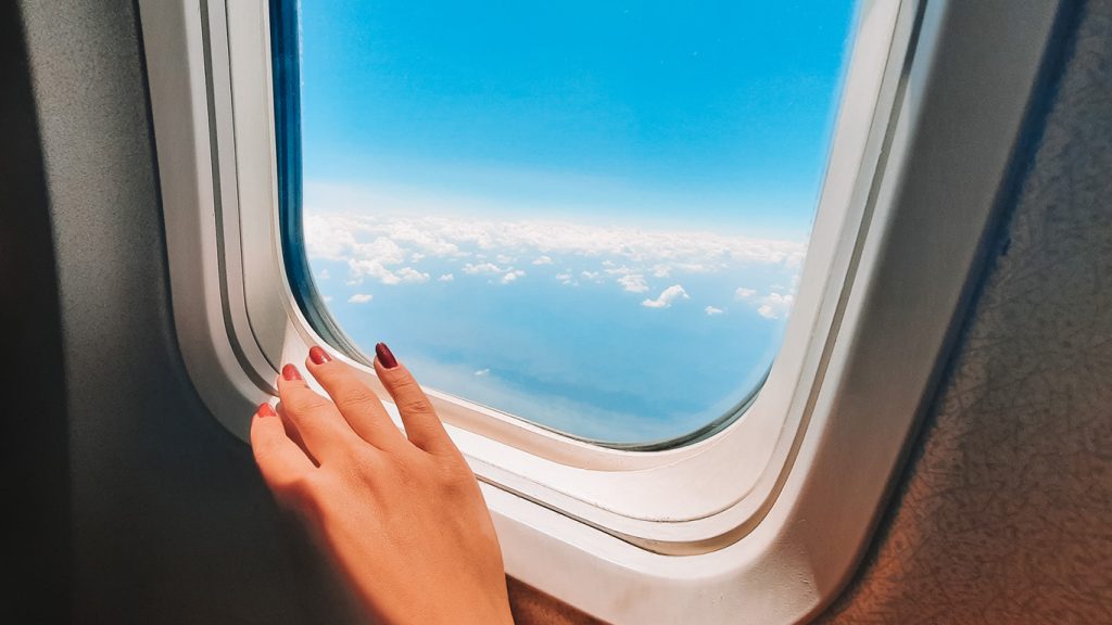Imagem da mão de uma mulher com unhas vermelhas, apoiada na janela de um avião, que é a melhor maneira como ir de Bogotá para Cartagena.