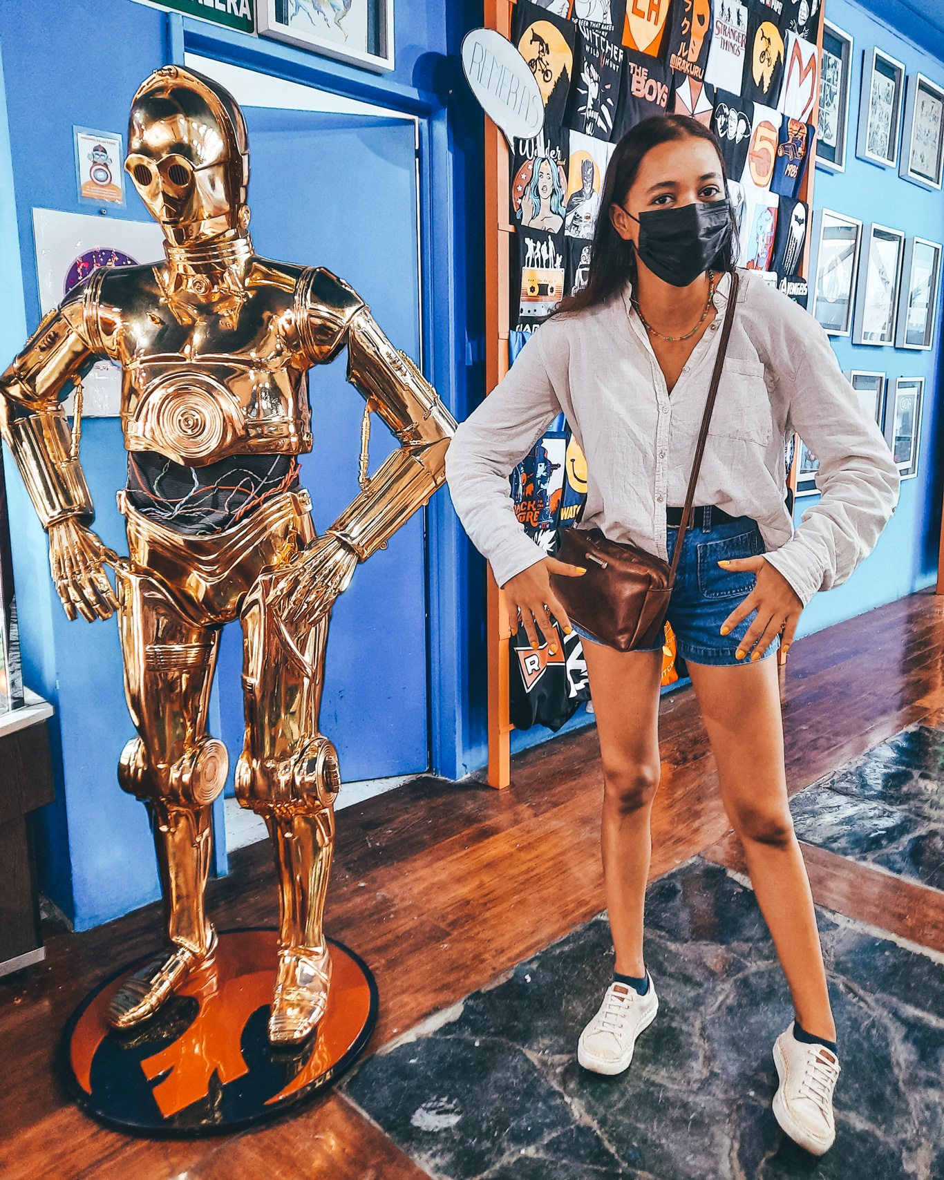 La-Revisteria-Buenos-Aires-1 Mulher posa imitando a posição de um boneco dourado do C-3PO, dentro de uma loja temática decorada com pôsteres geeks.
