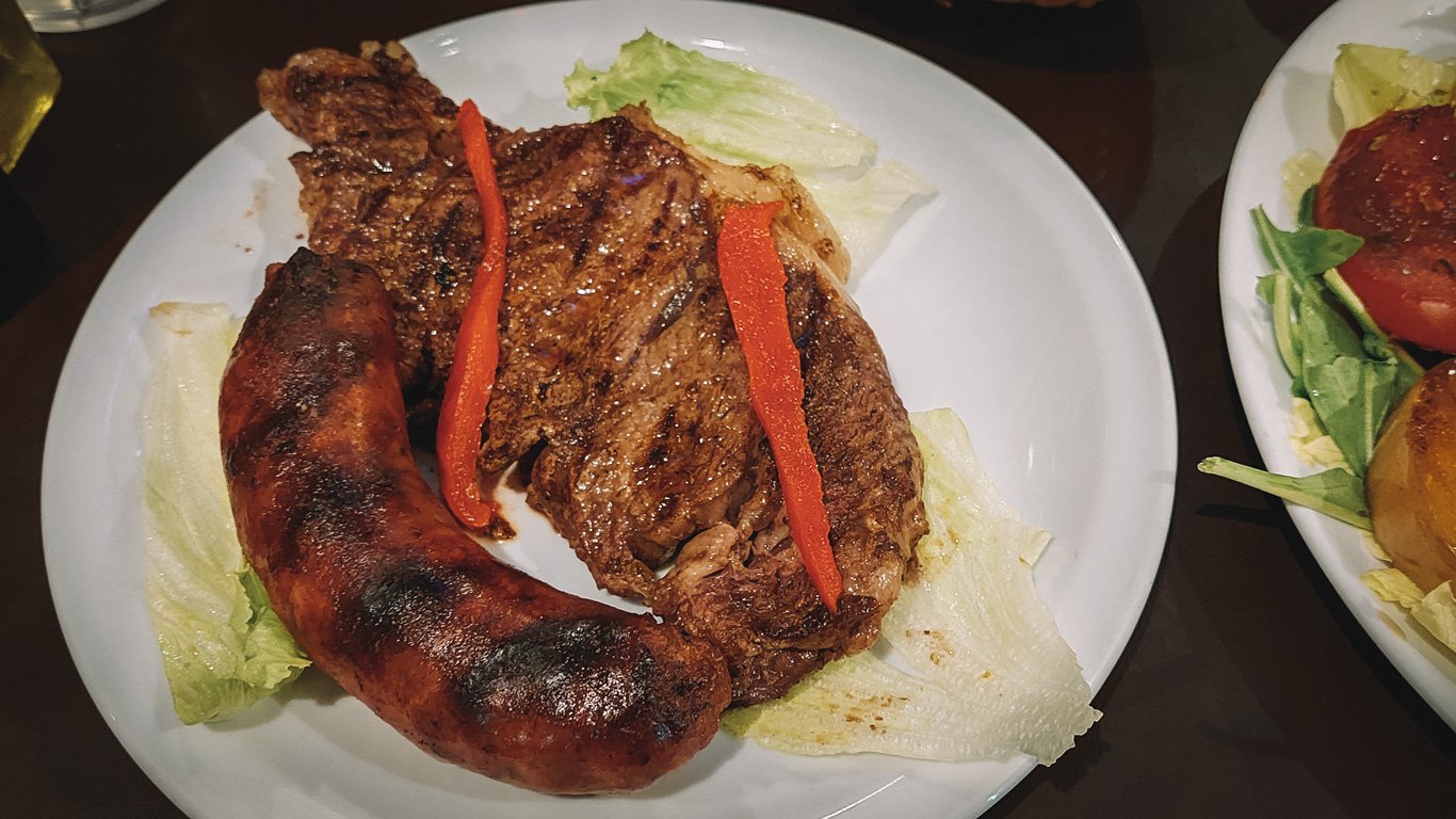 parrilla-argentina Tradicional parrilla argentina, composta por um suculento bife de chorizo e um chorizo, acompanhados de folhas e verduras assadas.