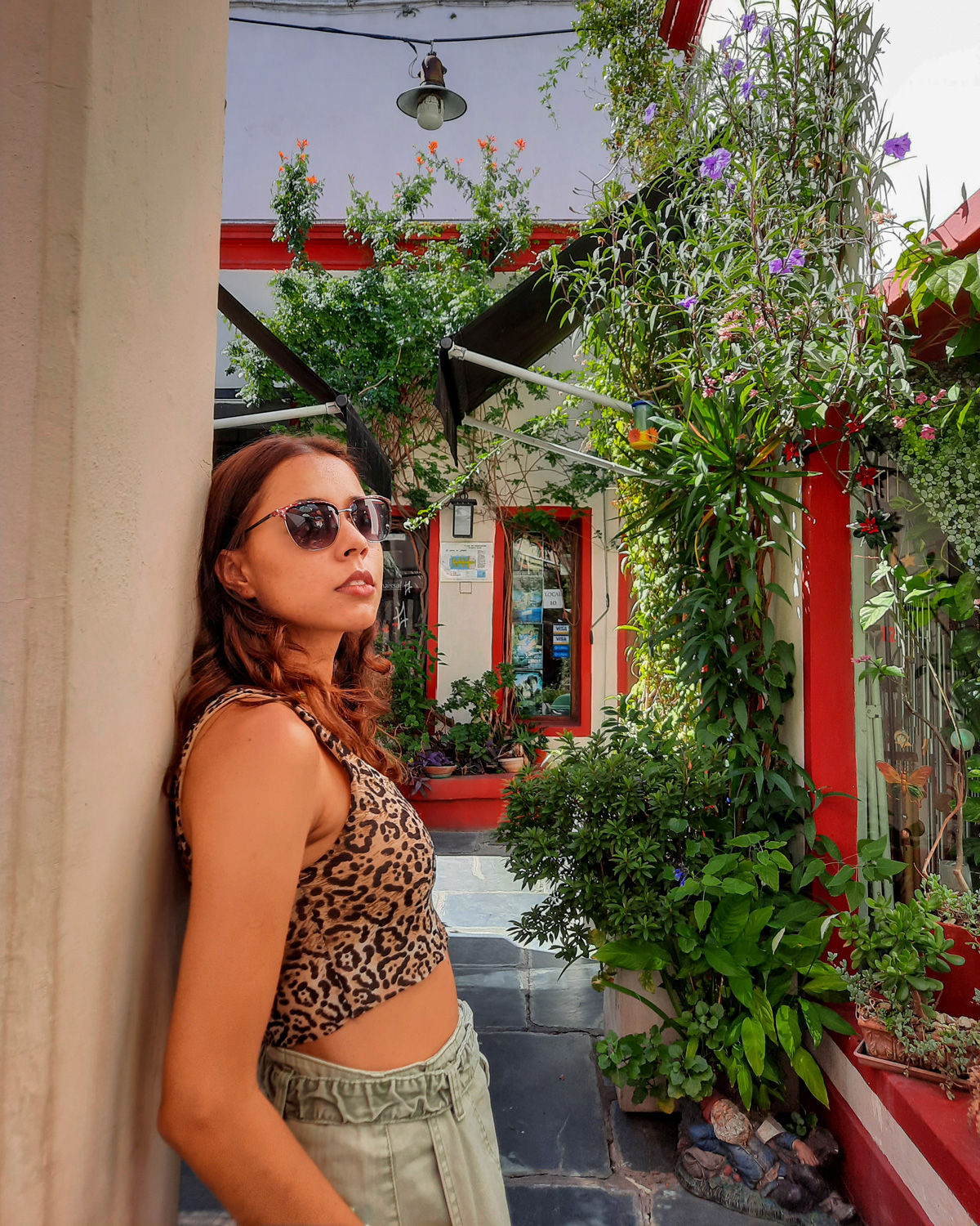 salar-french-1 Mulher encostada em parede de passagem estreita, na Galeria Solar de French em San Telmo, cercada por plantas e flores coloridas em vasos.