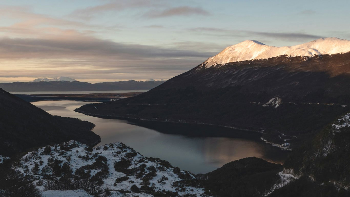lago-escondido-ushuaia Vista panorâmica do Lago Escondido entre montanhas cobertas de neve em Ushuaia, sob luz suave do amanhecer.