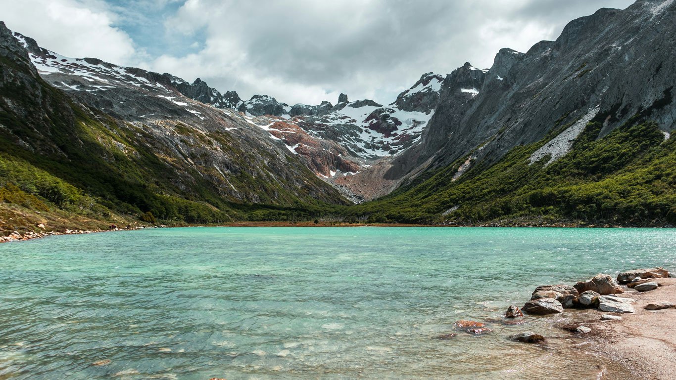 laguna-esmeralda-ushuaia Águas verde-esmeralda da Laguna Esmeralda cercadas por montanhas nevadas e vegetação densa nos arredores de Ushuaia.