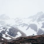 Duas pessoas caminhando por vale entre montanhas nevadas sob neblina densa em um centro invernal do Ushuaia, criando um clima misterioso e isolado.