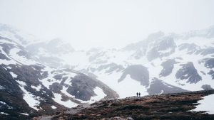 Duas pessoas caminhando por vale entre montanhas nevadas sob neblina densa em um centro invernal do Ushuaia, criando um clima misterioso e isolado.