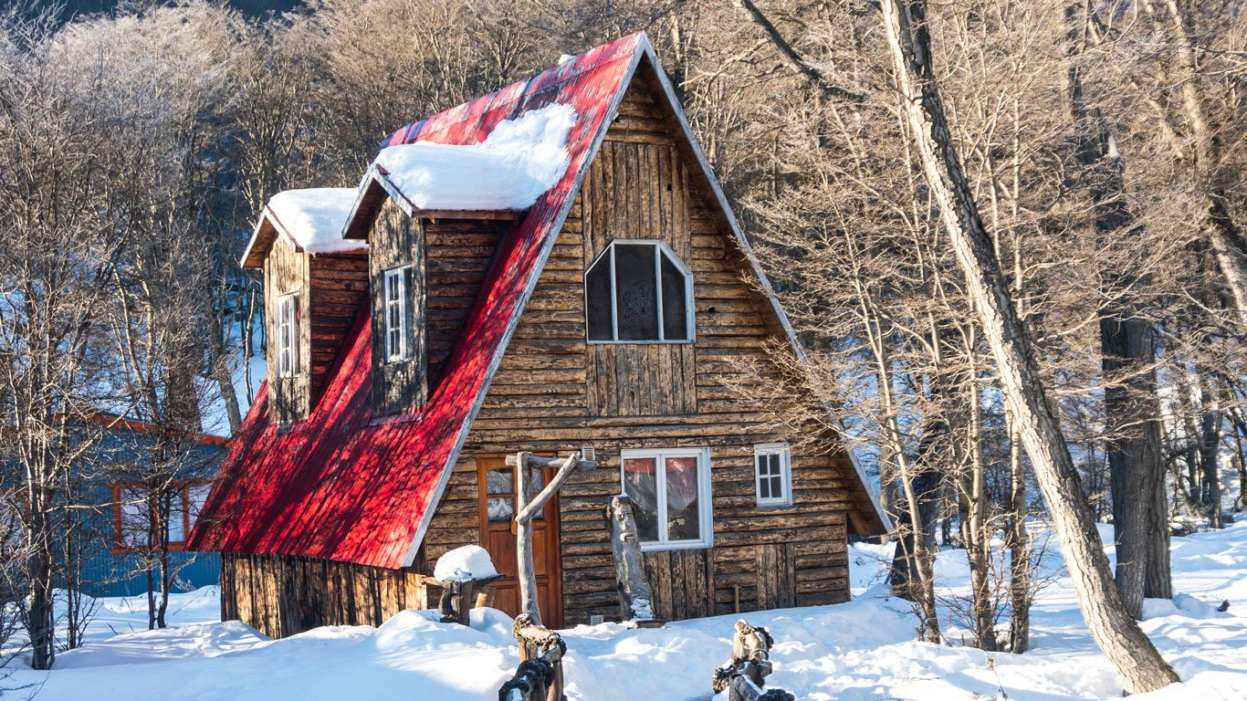 onde-ver-neve-en-ushuaia Pequena casa de campo vermelha em Ushuaia, com telhado nevado e cercada por neve.