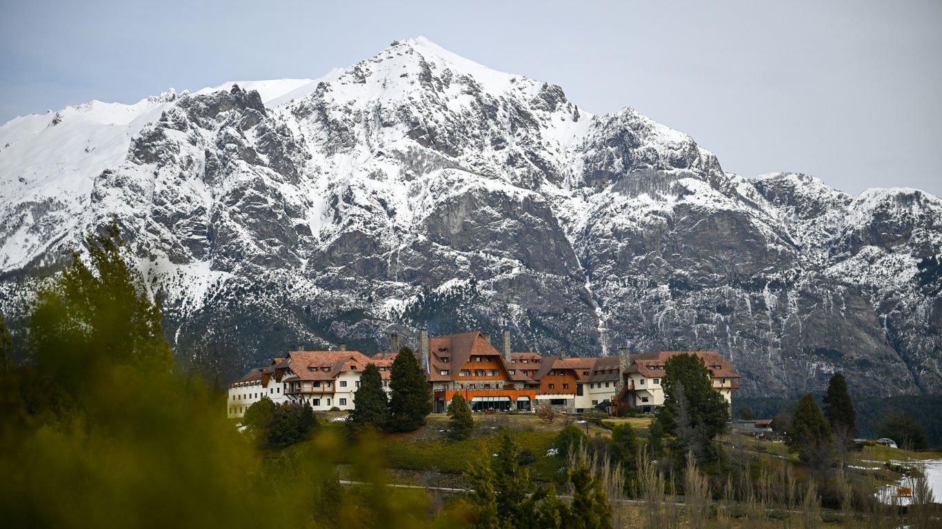 Vista panorâmica de uma imponente montanha coberta de neve com um grande hotel Llao Llao Resort, em Bariloche, rodeado por árvores e vegetação.