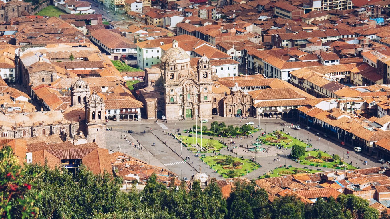 onde-ficar-em-cusco Praça central de Cusco com a Catedral e pessoas caminhando sob céu parcialmente nublado.