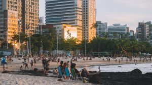 Vista deslumbrante do pôr do sol na Praia de Meireles, o melhor lugar onde ficar em Fortaleza, com o céu colorido em tons de azul, laranja e rosa, prédios altos ao fundo e pessoas aproveitando a praia.