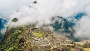 Vista panorâmica das ruínas de Machu Picchu envoltas por neblina e montanhas imponentes.