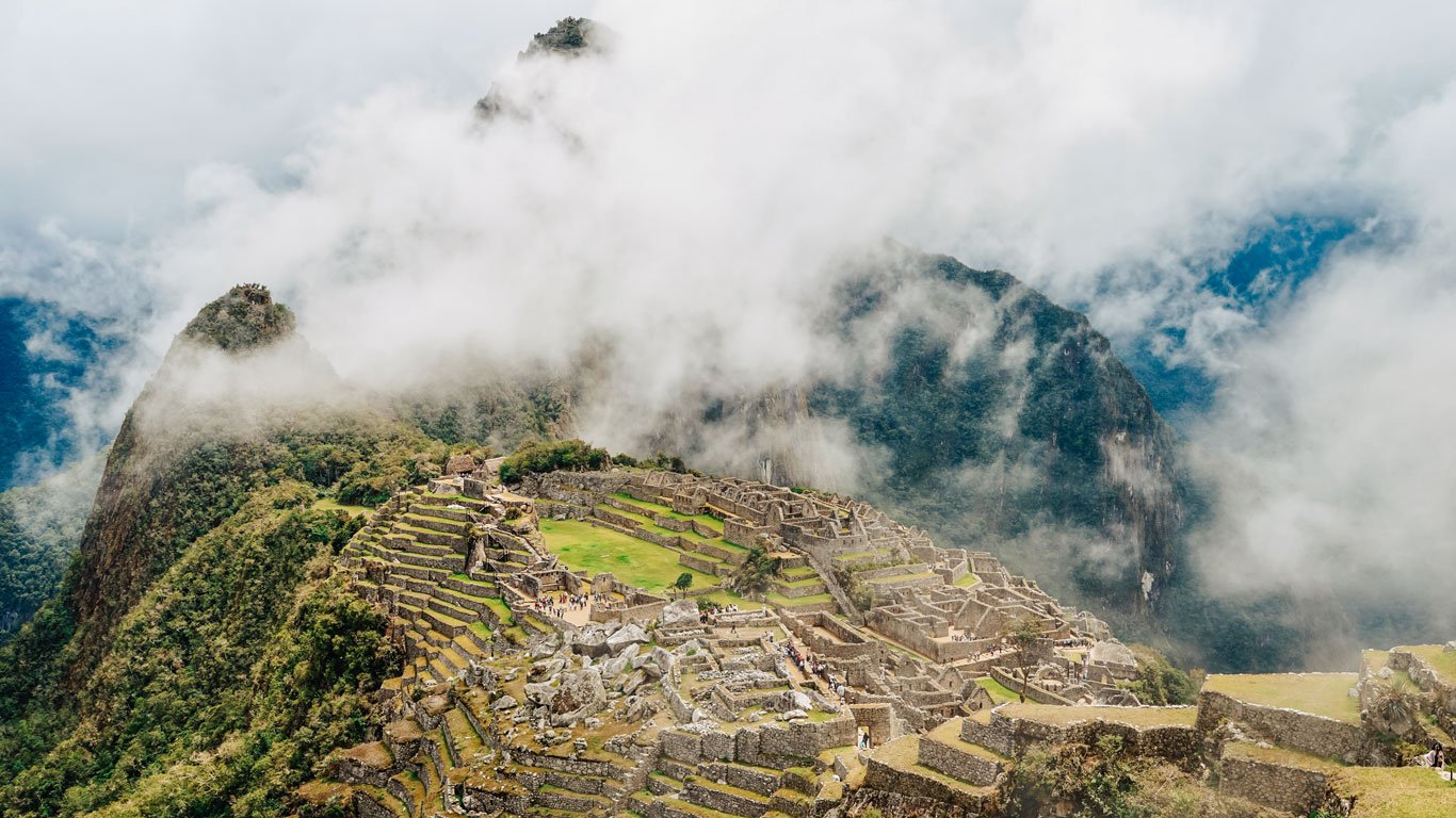 onde-ficar-em-machu-picchu-1 Vista panorâmica das ruínas de Machu Picchu envoltas por neblina e montanhas imponentes.