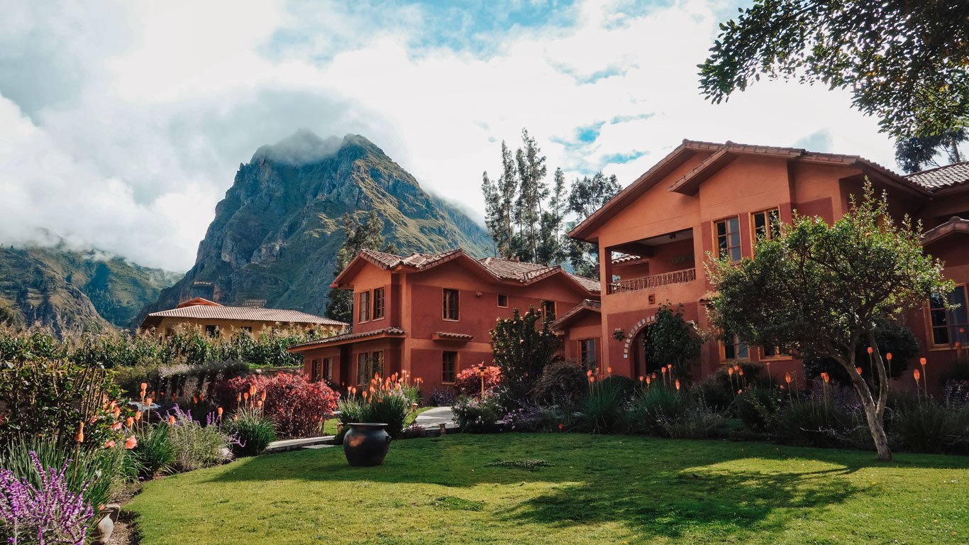 onde-ficar-no-valle-sagrado Hotel boutique no Vale Sagrado com jardins floridos e montanhas ao fundo, sob céu azul.