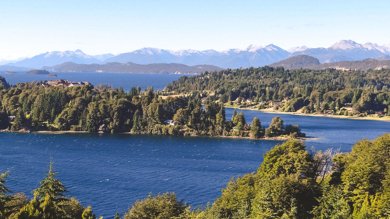bariloche-argentina-novembro Vista panorâmica de um lago azul profundo cercado por densas florestas e montanhas nevadas ao fundo em Bariloche em novembro, Argentina.