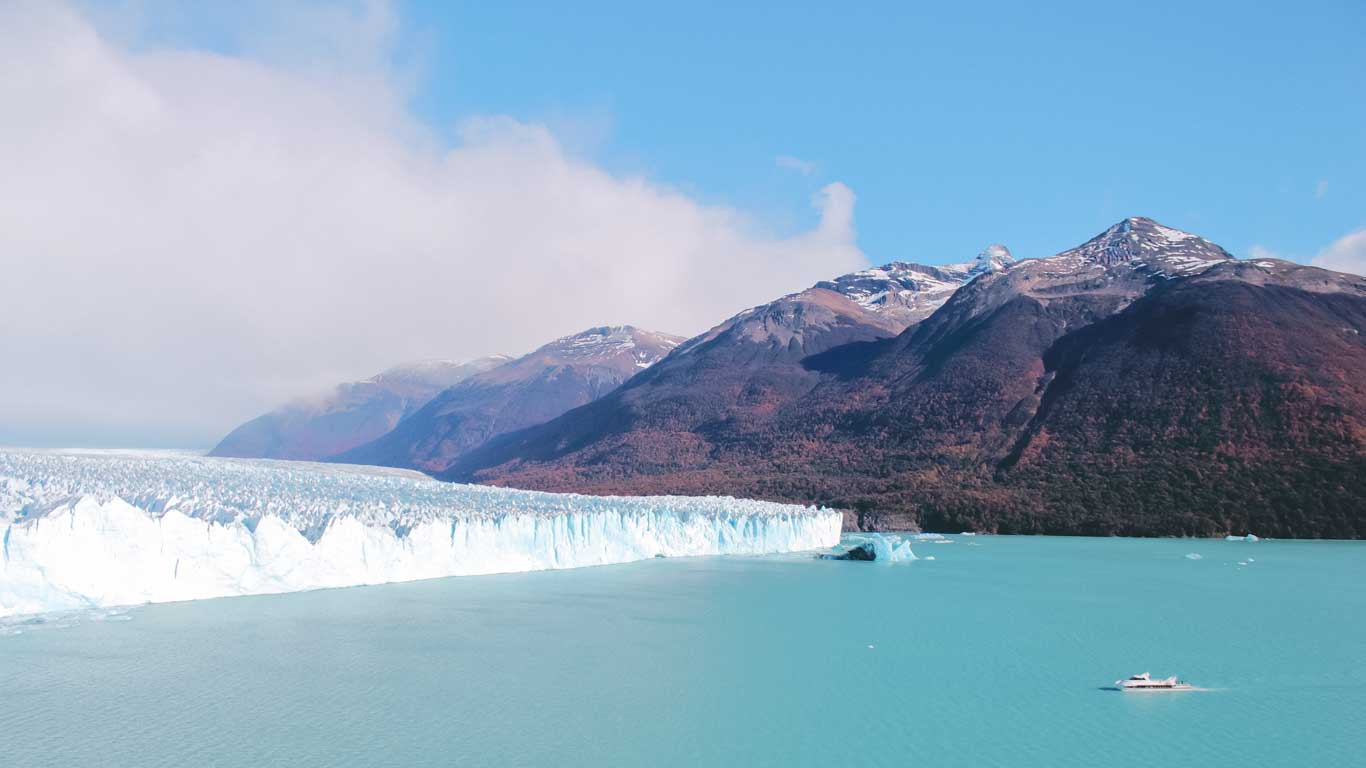 kayak por el glaciar Perito Moreno Glaciar Perito Moreno, a principal atração de El Calafate, em destaque, com enormes paredes de gelo azul claro que se estendem sobre o lago, cercado por montanhas nevadas e céu parcialmente nublado.