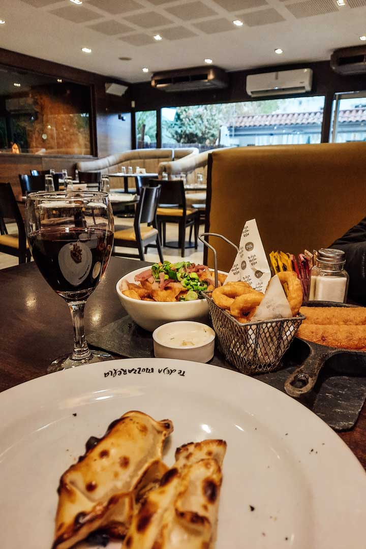 onde-comer-em-mendoza-zitto-1 Seleção de petiscos, incluindo empanadas argentinas, anéis de cebola e queijo empanado, acompanhado de vinho, servido no Zitto Bar e Grill em Mendoza.