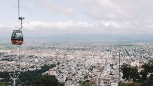 Imagem de Salta vista de um mirante com um bondinho em primeiro plano. A cidade se funde com o céu meio nublado no horizonte.