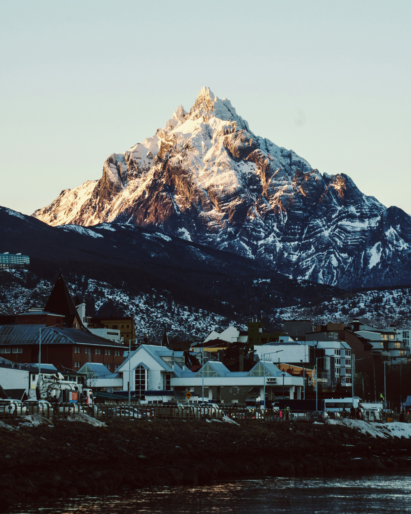 onde-ficar-em-ushuaia-1 Imagem do centrinho de Ushuaia com casas em madeira e montanhas cobertas de neve ao fundo.